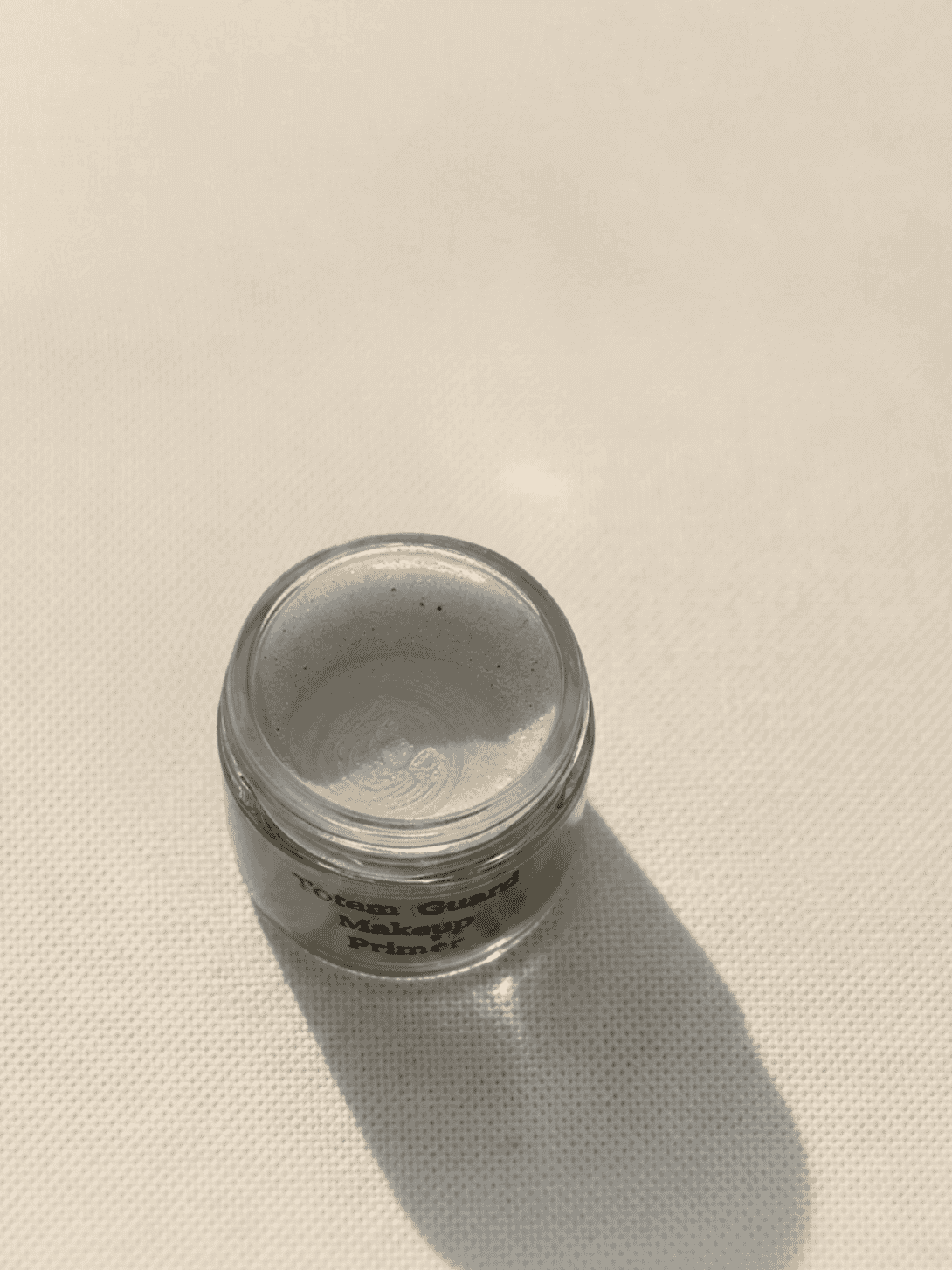 Glass jar showing the shimmering silver, light-reflective texture of Totem Guard Makeup Primer