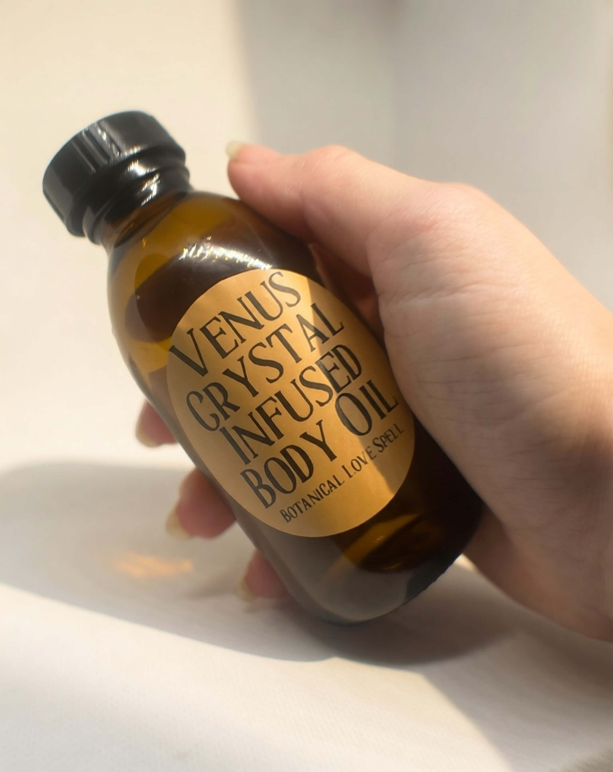 Holding Venus Crystal Infused Body Oil bottle against a clean neutral background